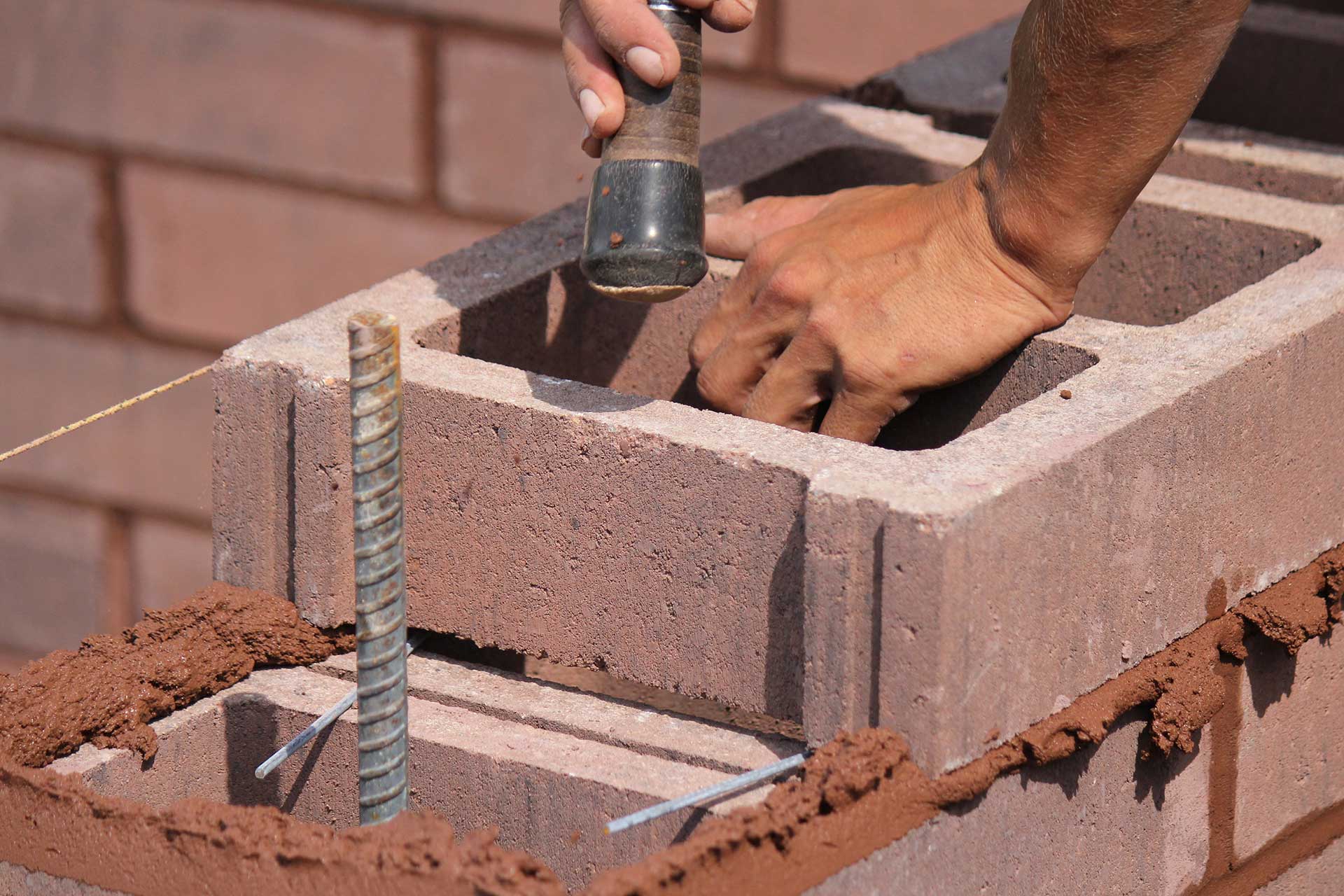 Mason setting colored concrete blocks in a wall under construction.