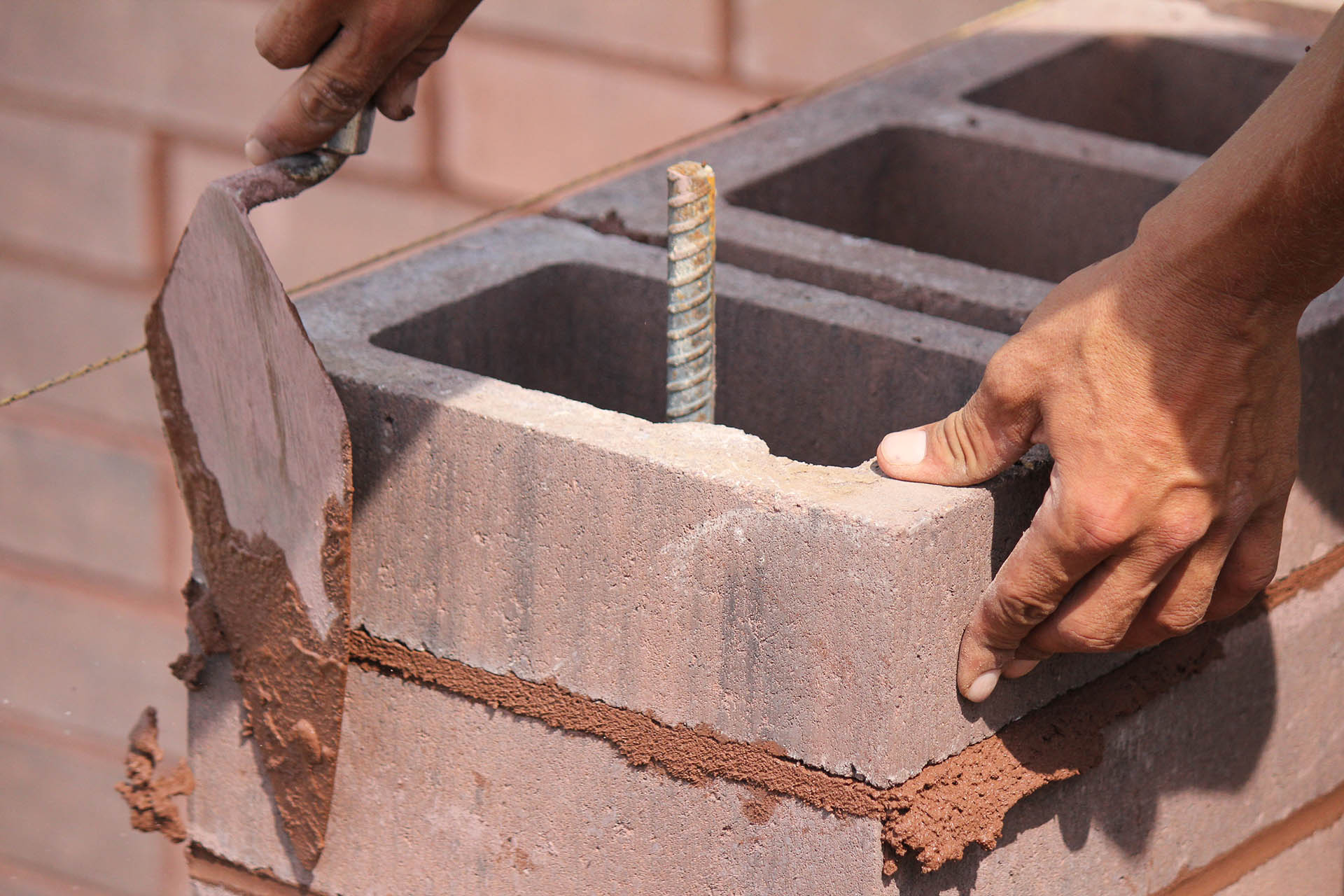 Close up of mason setting colored concrete blocks in a wall under construction.