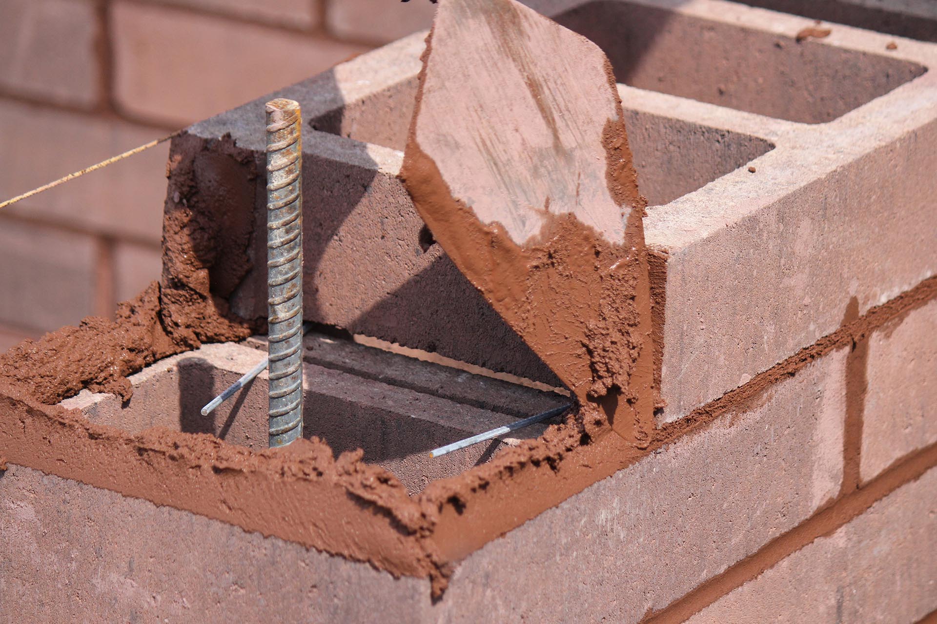 Mason setting colored concrete blocks in a wall under construction.